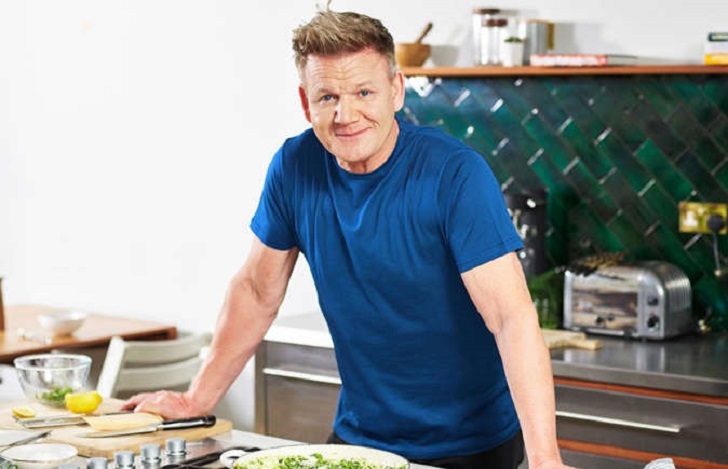 Gordon Ramsay prime rib recipe - Gordon cooking in a kitchen, smiling at the camera with cooking utensils and ingredients around him.